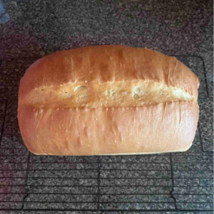 Overhead view of a golden brown loaf of bread cooling on a wire rack, featuring a professional center score and excellent oven spring.