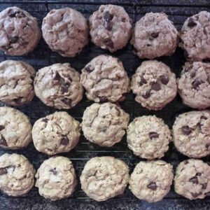 A wire cooling rack filled with 24 freshly baked peanut butter oatmeal chocolate chip cookies, showing a thick, chewy texture and melted chocolate bits.